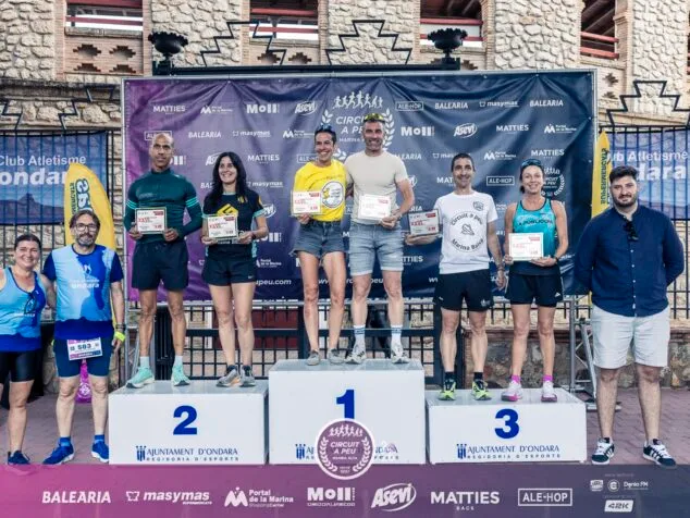 Fran López y María Isabel Ferrer dominan la XXVI Cursa Popular Ondara del Circuit a Peu Marina Alta 2026 16 Podio con tres corredores premiados sosteniendo trofeos y tres organizadores de pie a los lados, con un fondo de patrocinadores en la Cursa Popular Ondara.