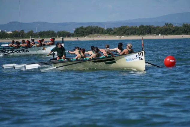 Imagen: Dos embarcaciones de remo con tripulaciones femeninas disputando una carrera en el mar cerca de la costa.