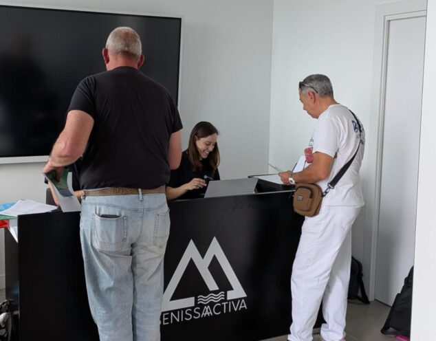 Benissa activa el reparto de tarjetas para sus nuevos contenedores inteligentes 2 Imagen: Dos hombres son atendidos por una mujer en un mostrador para recoger tarjetas de los nuevos contenedores en Benissa.