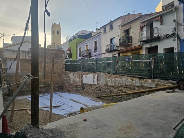 Imagen: Fotografía del solar de obras de la antigua Casa Beltrán en Calp, con el terreno excavado cubierto parcialmente por una lona blanca y edificios colindantes al fondo.