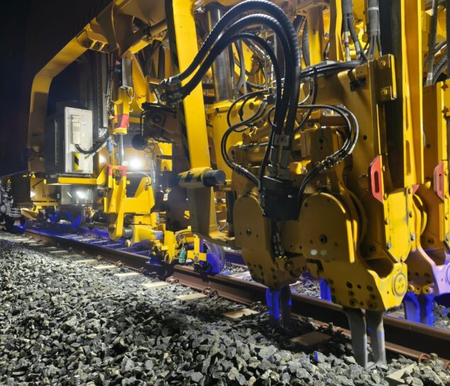 Imagen: Primer plano de maquinaria ferroviaria amarilla realizando trabajos de bateo en las vías del TRAM d'Alacant durante la noche.