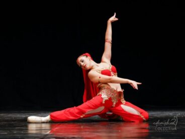 Bailarina de ballet con traje rojo actuando sobre un escenario oscuro.