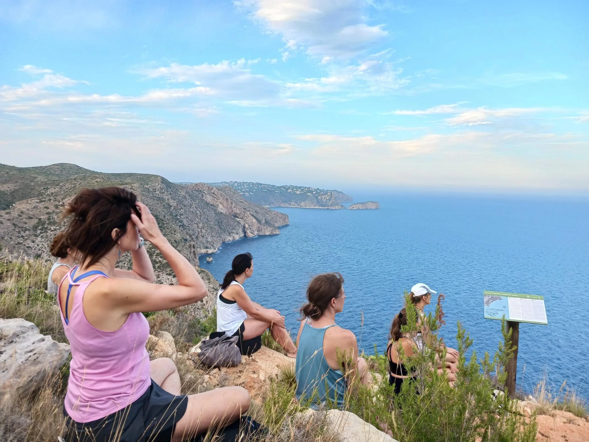 Grupo de personas sentadas en un acantilado mirando al mar durante una sesión del ciclo 'Respira l'estiu' en Benitatxell.