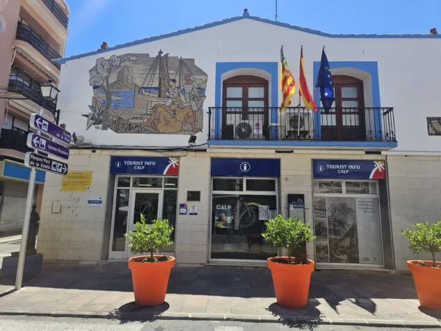 Imagen: Fachada del edificio Tourist Info Calp con el gran mosaico mural de Gastón Castelló situado sobre la entrada principal y las banderas oficiales en el balcón.