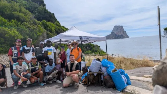 Imagen: Grupo de personas posando tras una limpieza de playa en Cala Manzanera, Calp, con bolsas de basura y una carpa del Ayuntamiento.