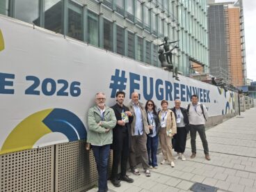 Siete personas de la delegación de Pedreguer posan frente a un gran cartel blanco con el texto '#EUGREENWEEK' y 'E 2026' en Bruselas.