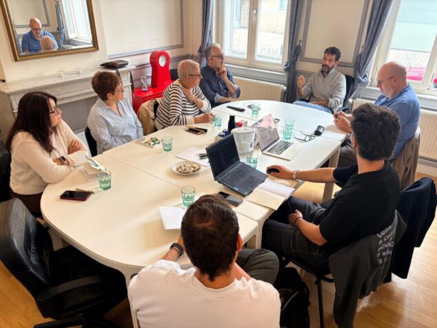 Imagen: Miembros de la delegación de Pedreguer sentados alrededor de una mesa con ordenadores portátiles durante una reunión.