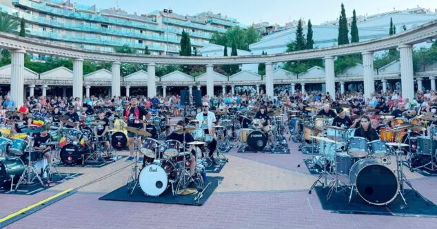 Imagen: Vista panorámica de un gran número de músicos tocando baterías simultáneamente en un anfiteatro al aire libre en Calp, rodeados de público y edificios.