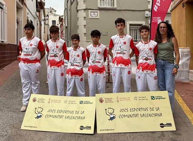 La Escola de Pilota d'Ondara brilla en los JECV con dos oros y tres medallas más en las finales autonómicas 1 Imagen: Seis jóvenes jugadores de pilota de Ondara con uniforme rojo y blanco y medallas, posan junto a una mujer y carteles de los Jocs Esportius.
