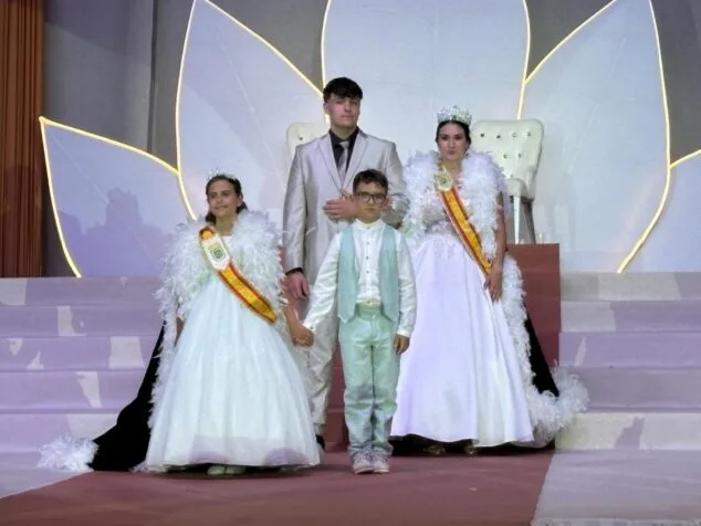 Foto de cuatro jóvenes, dos chicas con bandas de reina y dos chicos, en un escenario decorado para una gala de fiestas en Calp.