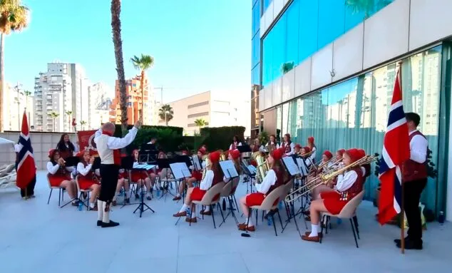 La banda femenina noruega Haslum Skoles Jentekorps, con trajes tradicionales y banderas de Noruega, toca instrumentos de viento al aire libre en Calp.
