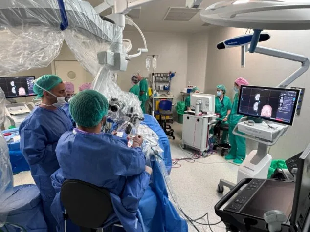 El Hospital de Dénia realiza una pionera cirugía cerebral de alta complejidad con monitorización neurofisiológica 1 Imagen: Equipo médico en quirófano realizando una neurocirugía con microscopio y monitores de visualización.
