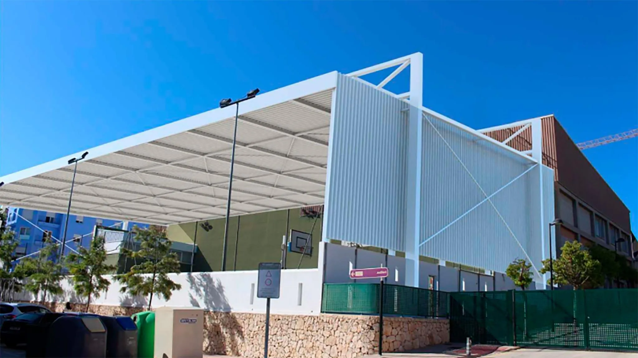 Instalación deportiva municipal cubierta en Teulada con pista polideportiva y canasta de baloncesto bajo cielo azul.
