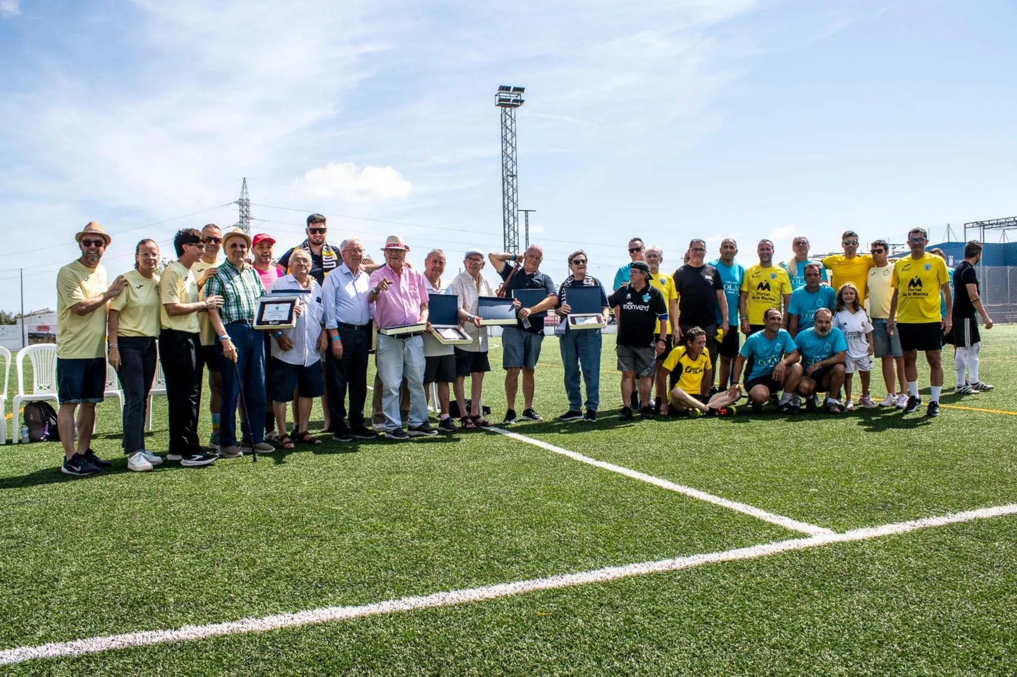 Numeroso grupo de personas posando en un campo de fútbol, algunos sosteniendo placas conmemorativas, durante la Jornada Grogueta de la UD Ondarense.