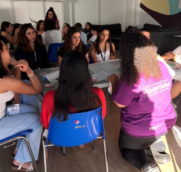 Imagen: Jóvenes sentados alrededor de una mesa con papeles y bolígrafos, participando en un debate o taller.