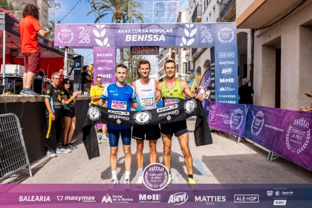 Imagen: Tres corredores masculinos posan sonrientes en la zona de meta de la Cursa Popular Benissa sujetando una pancarta del Circuit a Peu.