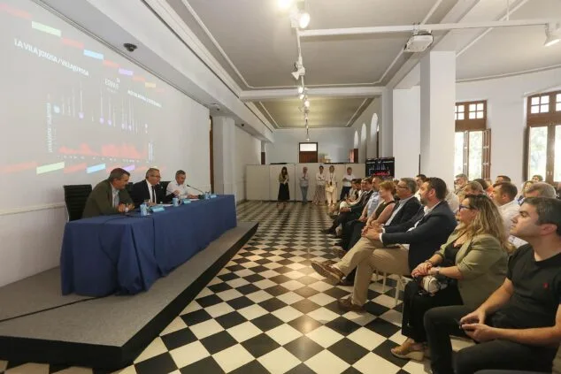 Imagen: Toni Pérez, Javier Guillén y otro ponente sentados en una mesa durante una rueda de prensa, con una pantalla gigante detrás mostrando un gráfico del recorrido ciclista.