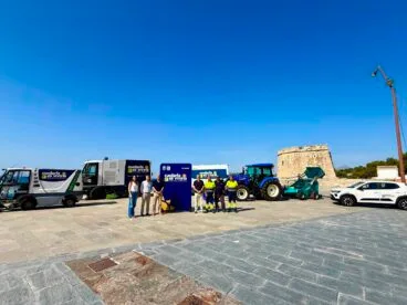 Presentación de la nueva flota de vehículos de limpieza del Ayuntamiento de Teulada Moraira con autoridades y trabajadores frente a una torre histórica.