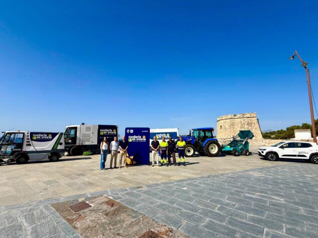 Imagen: Presentación de la nueva flota de vehículos de limpieza del Ayuntamiento de Teulada Moraira con autoridades y trabajadores frente a una torre histórica.