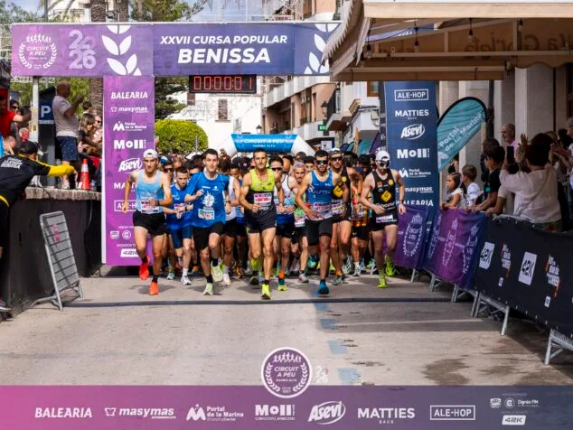 Imagen: Salida multitudinaria de la carrera popular en Benissa con atletas corriendo bajo un arco inflable.