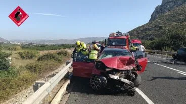 Bomberos trabajando sobre un coche rojo siniestrado tras un accidente de tráfico en la carretera N-332.