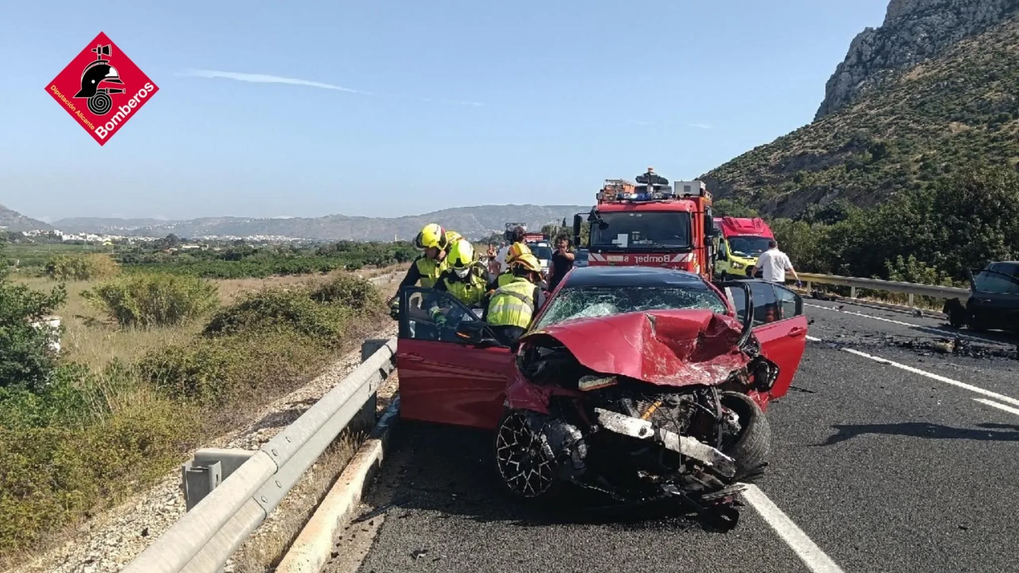 Bomberos trabajando sobre un coche rojo siniestrado tras un accidente de tráfico en la carretera N-332.