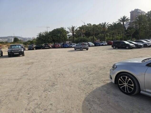 Imagen: Varios coches aparcados en una gran explanada de tierra y grava rodeada de vegetación en Calp.