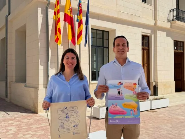 Celia Ausias y Arturo Poquet sostienen un cartel y una bolsa con la imagen de la campaña de empadronamiento de Benissa frente al ayuntamiento.