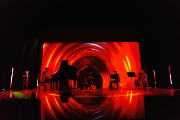 Immagine: Palco del concerto 'Colors del So' a Calp con musicisti che suonano i loro strumenti e suggestive proiezioni di luce rossa.