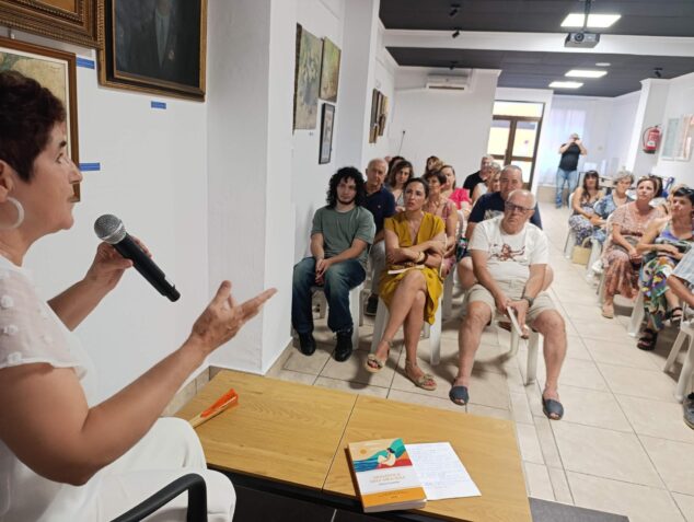 'Gramática de los girasoles' de Elvira Cambrils llega a Ondara 4 Imagen: Elvira Cambrils hablando con un micrófono durante la presentación de su libro 'Gramática de los girasoles' frente a un público sentado.