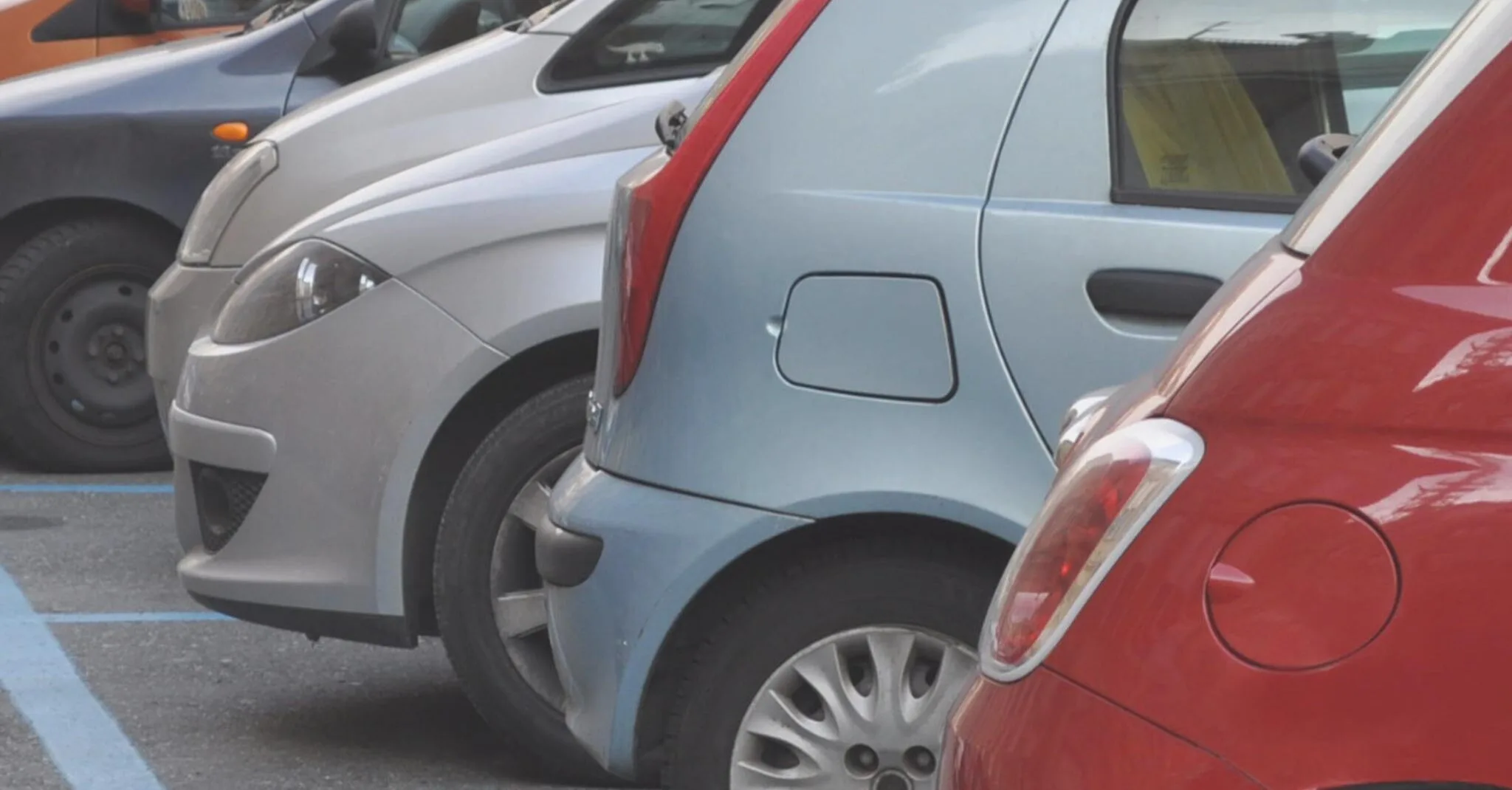 Fila de coches aparcados en batería en una zona de estacionamiento regulado marcada con líneas azules.