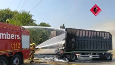 Bomberos extinguiendo con mangueras un incendio en el remolque abierto de un camión en una carretera.