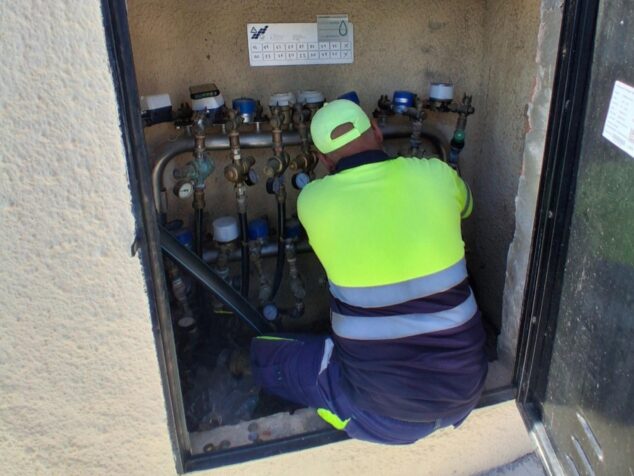 Imagen: Un técnico con chaleco amarillo instala contadores de agua inteligentes en una arqueta de registro.