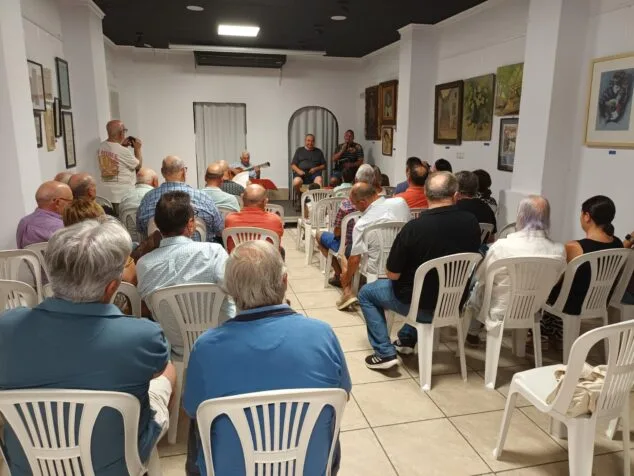 Imagen: Joan Mestre y Jovi Lozano-Seser sentados al frente durante la presentación del libro "Gala balsámica", con un guitarrista y público.