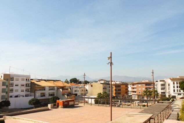 Imagen: Vista de la Plaza de VI Centenari en Teulada, con suelo pavimentado y pocos árboles bajo un cielo soleado.