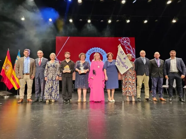 Imagen: Grupo de personas en un escenario, algunas sosteniendo premios y una bandera, con una pantalla de fondo que dice '9 D'OCTUBRE'.