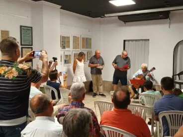 Joan Mestre presenta su séptimo poemario 'Gala balsàmica' en la Associació Cultural Ocell de Ondara 6 Varios protagonistas de pie y un guitarrista sentado durante una presentación literaria ante un público.