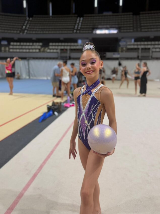 Sophie O'Reilly, del Club Les Marines de Calp, Campeona de España de gimnasia rítmica en pelota 10 Sophie O'Reilly, gimnasta rítmica del Club Les Marines, sonríe a cámara sosteniendo una pelota en un pabellón deportivo.