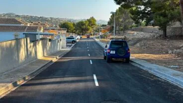 Vial de acceso a la urbanización Balcón de Bernia recién reconstruido y asfaltado, con un coche azul aparcado.