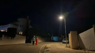 Ana Sala y Pere Moll caminando de noche bajo una nueva farola solar encendida en una calle de Calp.