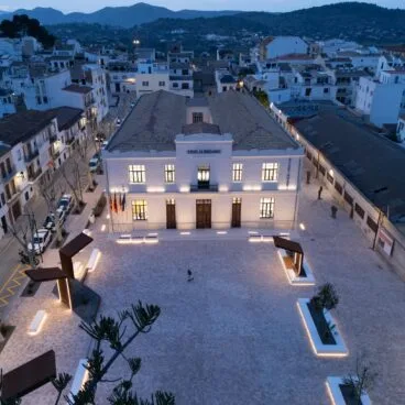 Vista aérea nocturna de la fachada iluminada del edificio del Ayuntamiento de Benissa y su plaza.