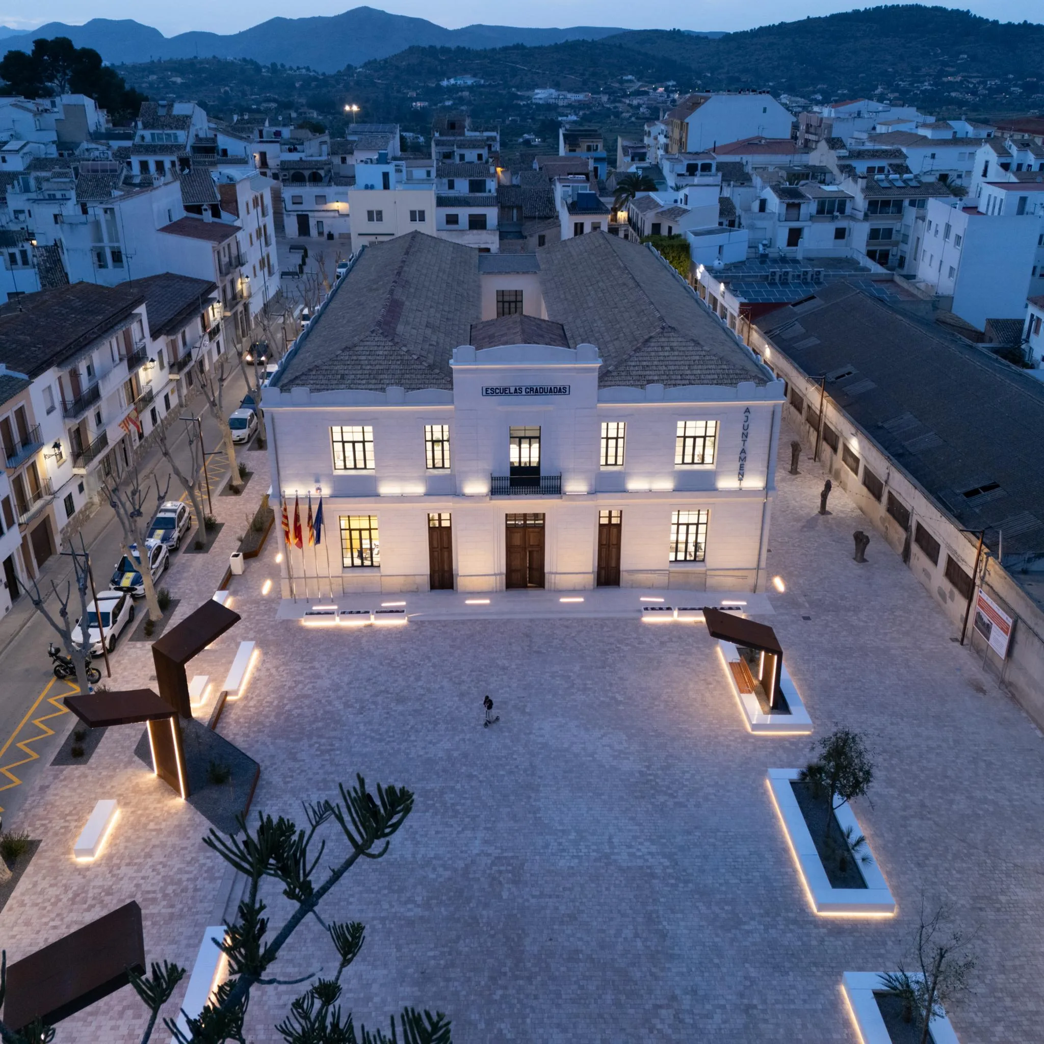 Vista aérea nocturna de la fachada iluminada del edificio del Ayuntamiento de Benissa y su plaza.