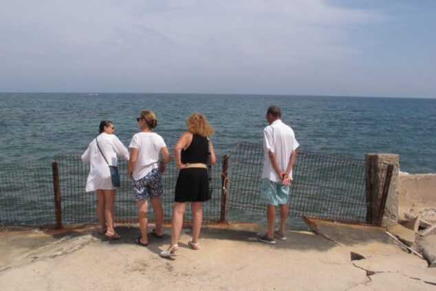 Imagen: Cuatro personas miran al mar desde una zona costera rocosa con una valla dañada en Dénia.