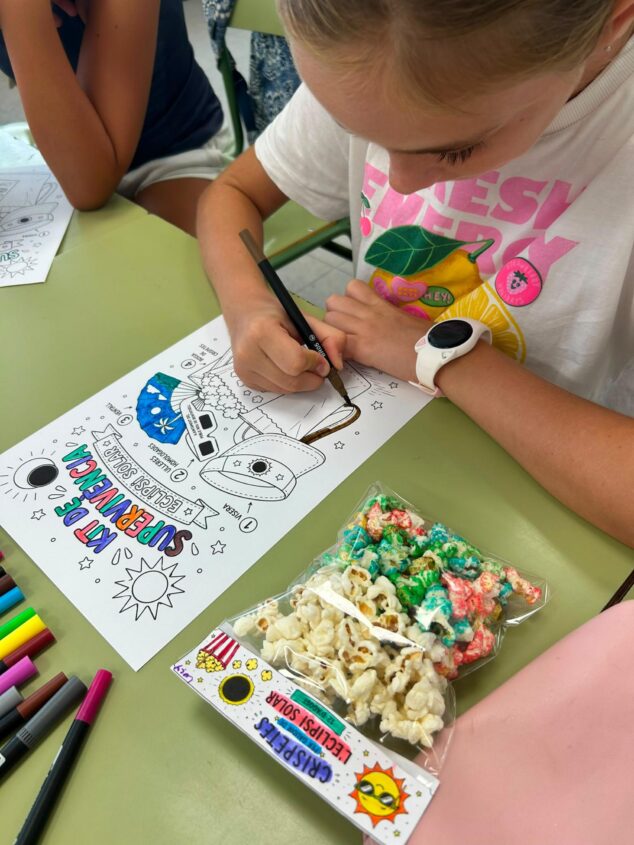 El «Kit de supervivencia» que convierte el eclipse de 2026 en una aventura en Benitatxell 1 Imagen: Una niña colorea una ficha educativa sobre el kit del eclipse solar en una mesa escolar.
