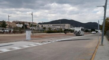 Una autocaravana blanca aparcada en una plaza señalizada del área municipal de Pego, con una torreta de servicios visible.