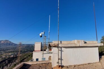 Benitatxell refuerza la prevención de incendios con sensores inteligentes y una red LoRaWAN 2 Antenas, cámara de vigilancia y equipamiento tecnológico instalados en la azotea de un edificio con un paisaje montañoso de fondo.