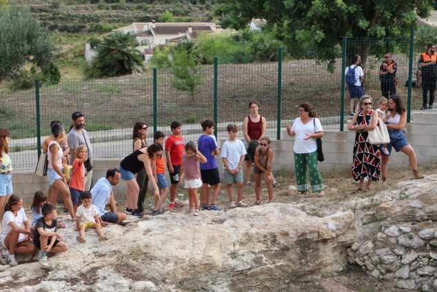 Imagen: Un grupo de adultos y niños escucha a una guía junto a un yacimiento arqueológico en la Cova de les Bruixes de Benitatxell.