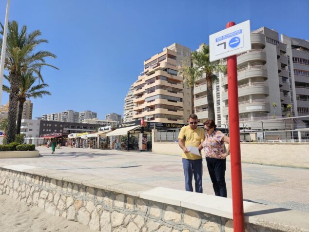Imagen: Señal de zona de fumadores en el paseo marítimo de la playa de Calp con dos personas consultando un documento a su lado.