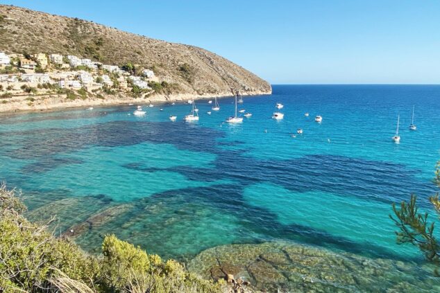 Imagen: Vista panorámica de la playa El Portet en Moraira con barcos fondeados y aguas turquesas.