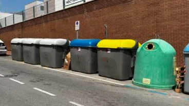Fila de contenedores de basura y reciclaje de distintos colores en una calle de Calp.